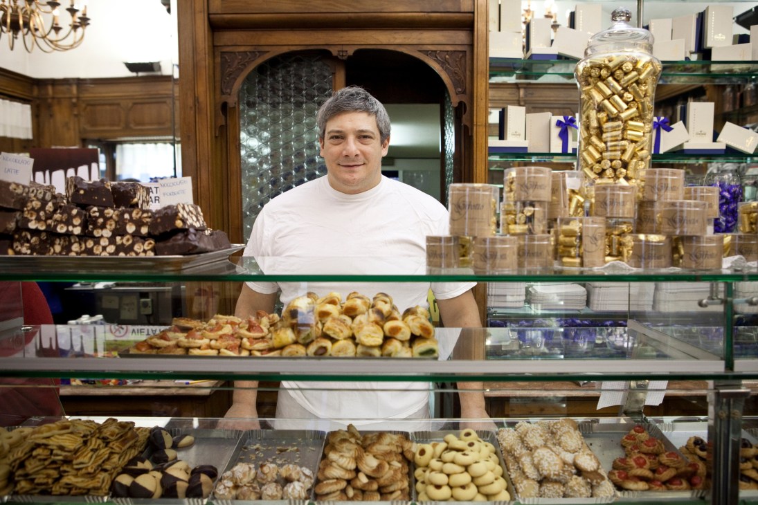 Man standing behind pastry counter displaying fresh baked goods at Gertosio café in Turin