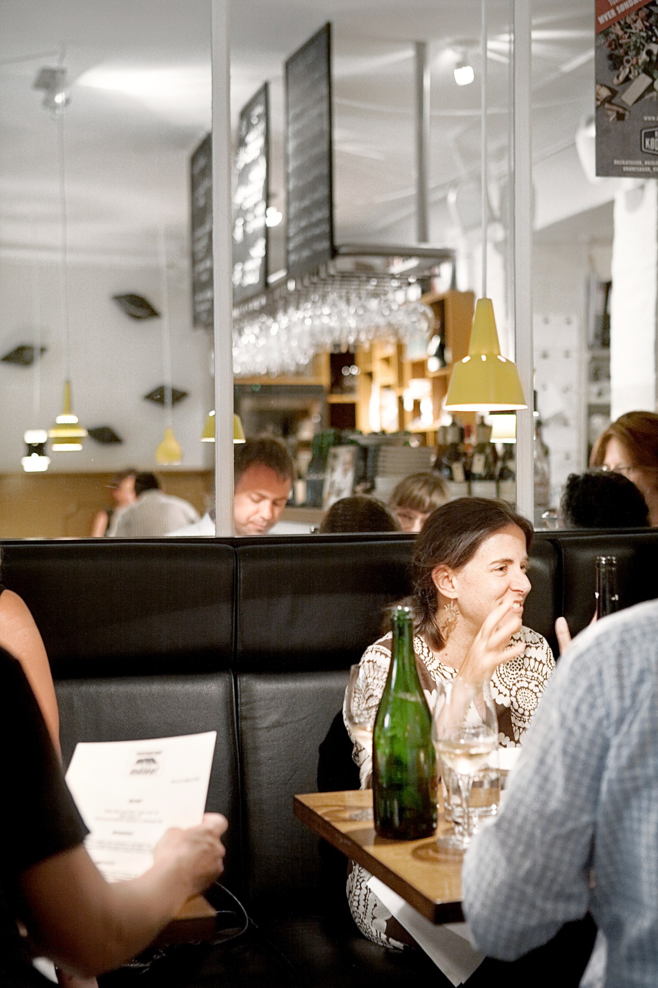 Diners seated at Mêlée French bistro in Copenhagen with menus and beer bottles on tables.