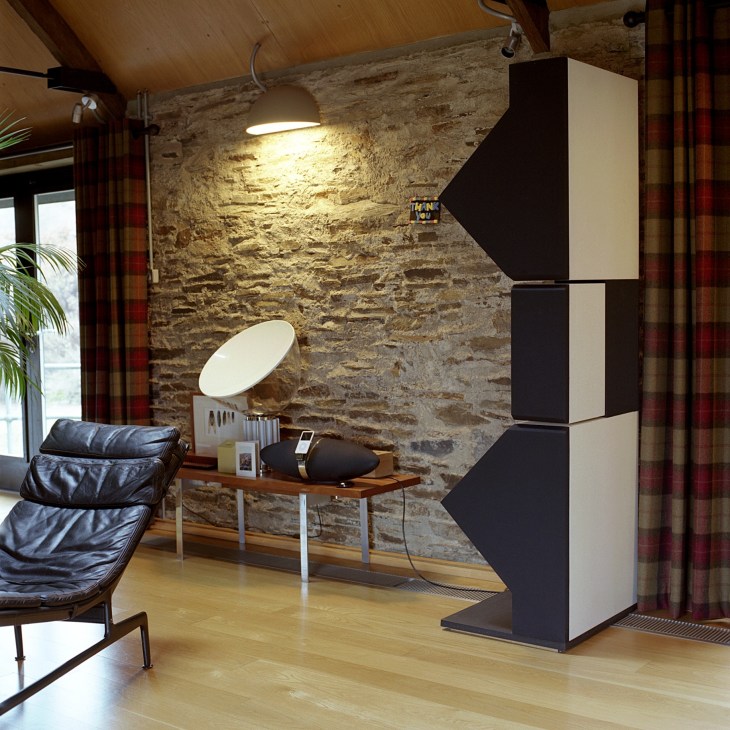B&W 900 series speakers in a modern living room with stone walls and contemporary furniture.