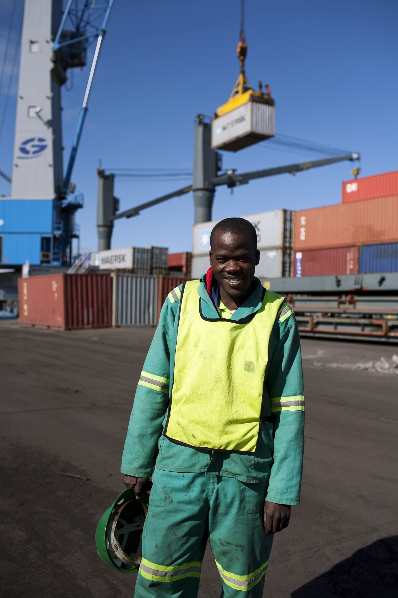 Port worker in high-visibility gear at Port Maputo with shipping containers and yellow crane in background.