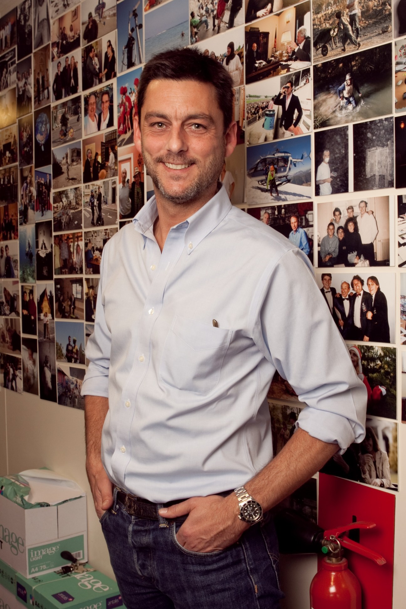 Photographer Alvaro Canovas smiles at the camera in a light blue shirt against a wall of photographs.