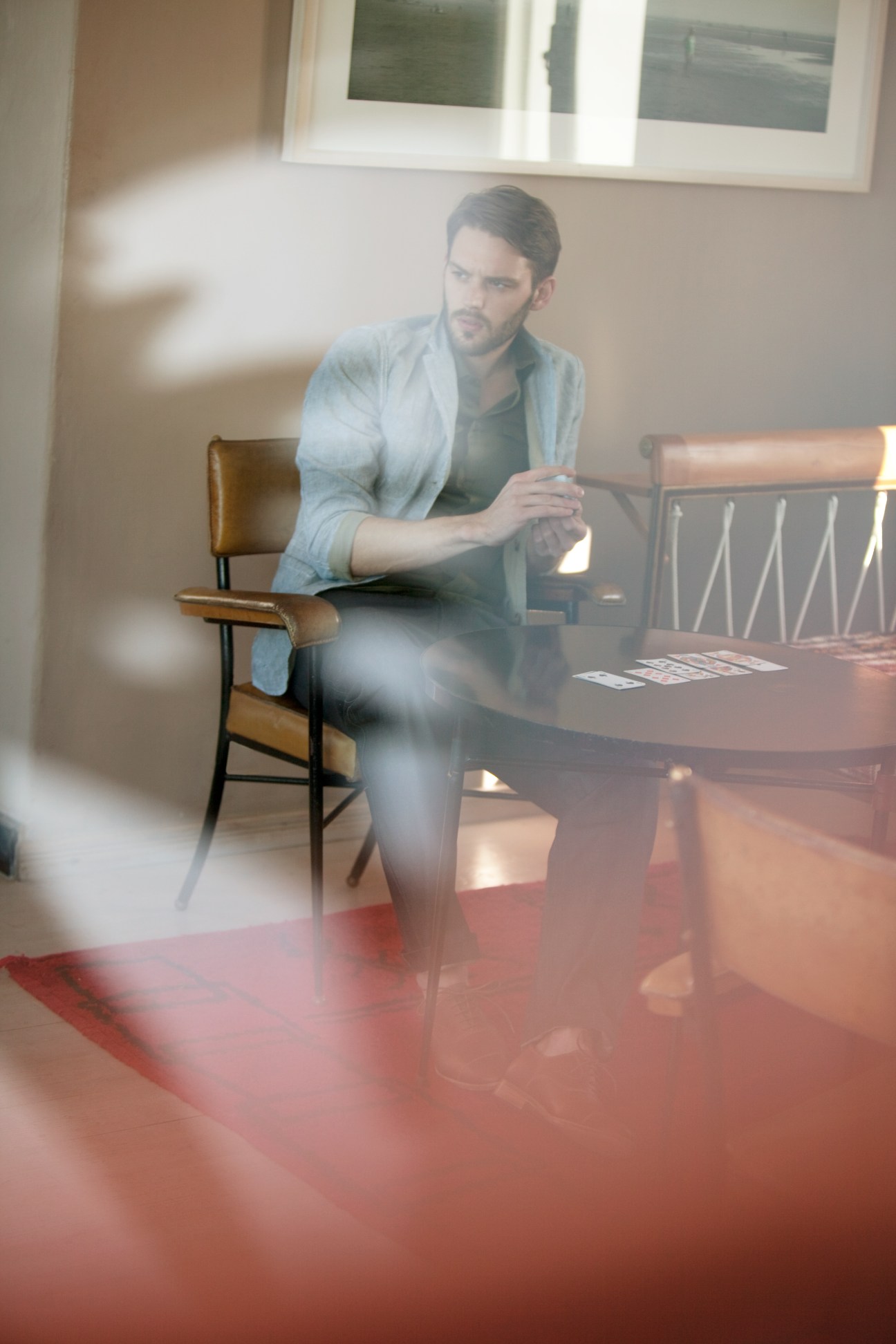 Man wearing light blue Beams+ jacket and Prada shirt seated at table in modern interior.