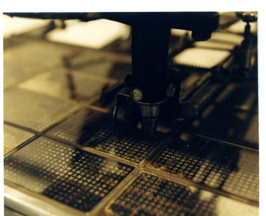 Close-up of a printing head scanning over glass plates containing Japanese characters and fonts.