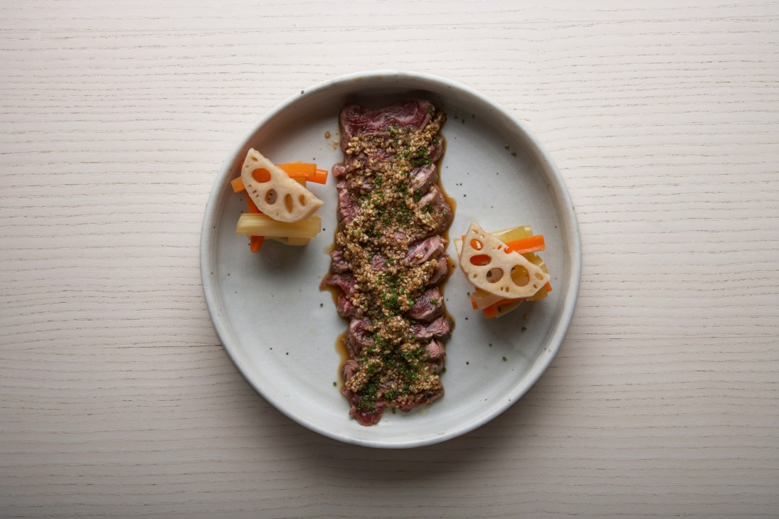 Aged rib-eye beef tataki with sesame dressing and lotus root slices on a white plate.