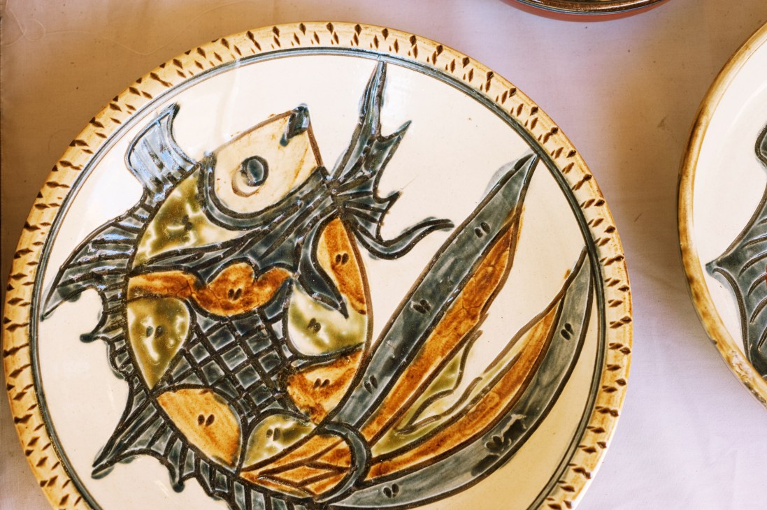 Hand-painted Tsuboya ceramic plate featuring a stylized fish in black, orange, and yellow with decorative border.