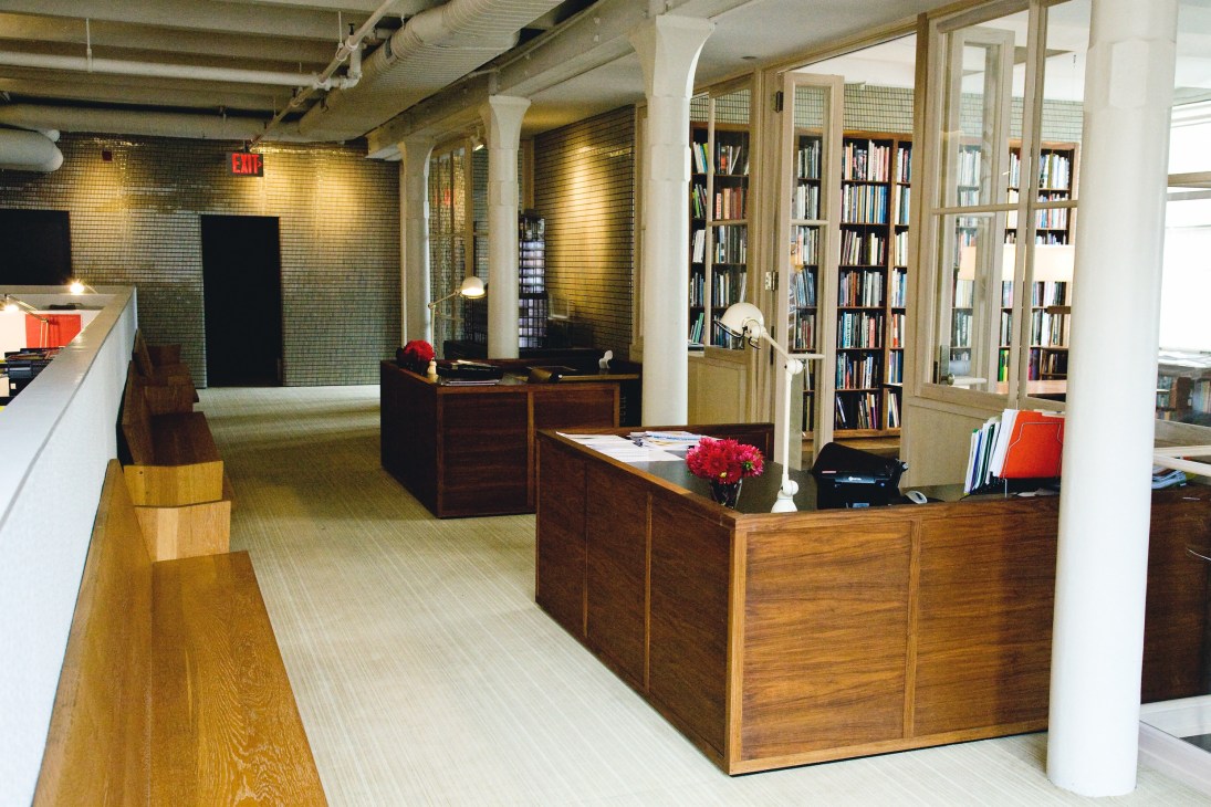 André Balazs Properties New York office interior with wooden desks, bookshelves, brick walls and red flowers.