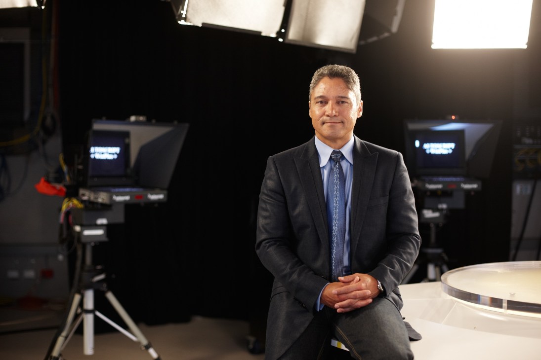 Anton Enus, presenter of 'World News Australia', sits in an SBS television studio with cameras and lighting equipment visible in the background.