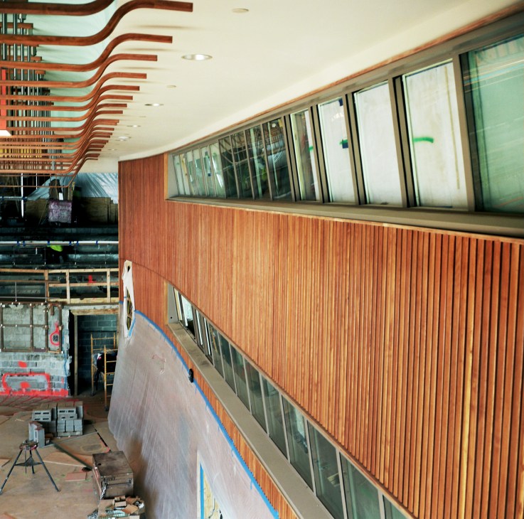 Mid-century modern interior with sculptural wooden ceiling beams and ash wood panelling during restoration.