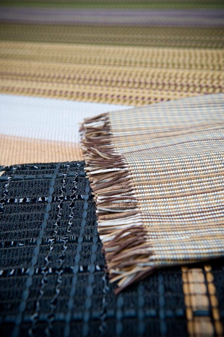 Close-up of finished woven leather samples in various colors showing detailed textile patterns and frayed edges.