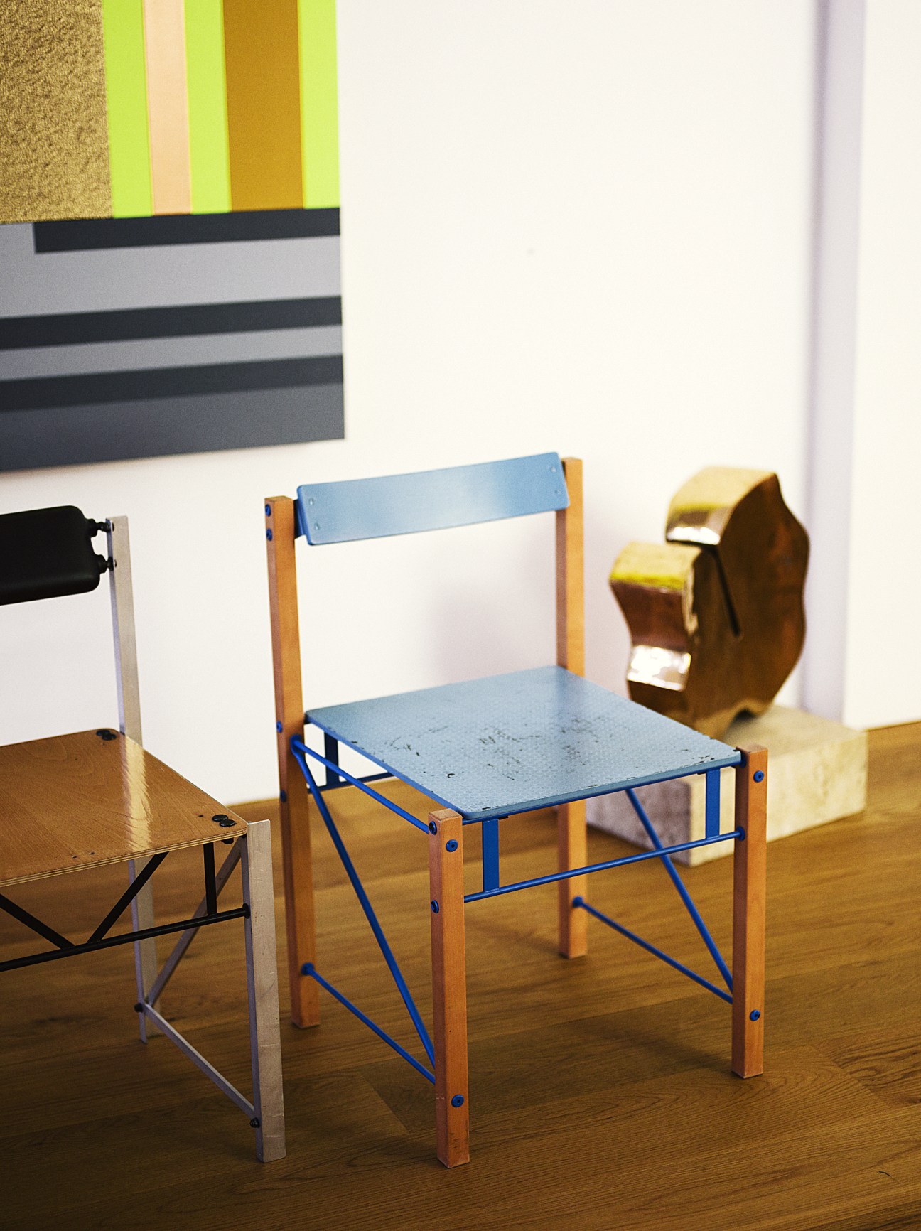 Handmade chairs by Yrjö Kukkapuro with blue seats and wooden frames displayed on wooden floor with colorful artwork above.