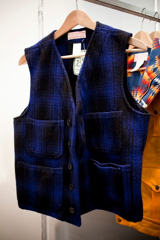 Blue and black plaid wool waistcoat on wooden hanger displayed at Filson booth.
