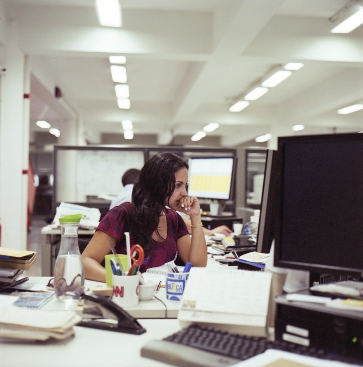 A woman journalist at her desk in the Folha de S.Paulo newsroom, surrounded by papers and office supplies.