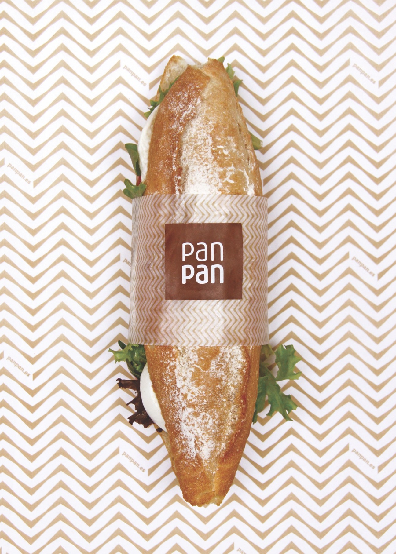 PanPan bakery sandwich wrapped in branded paper with chevron wheat pattern against geometric background.