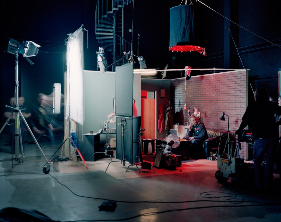 Night-time film set with red brick building, professional lighting rigs, and crew members working on production.