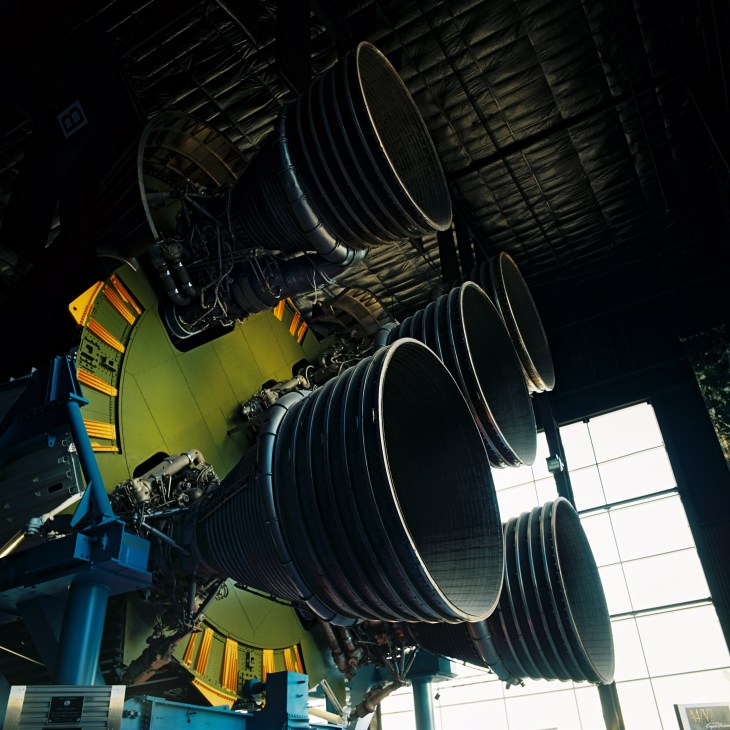 Large black cylindrical rocket engines of the Saturn V displayed inside a museum with industrial ceiling.