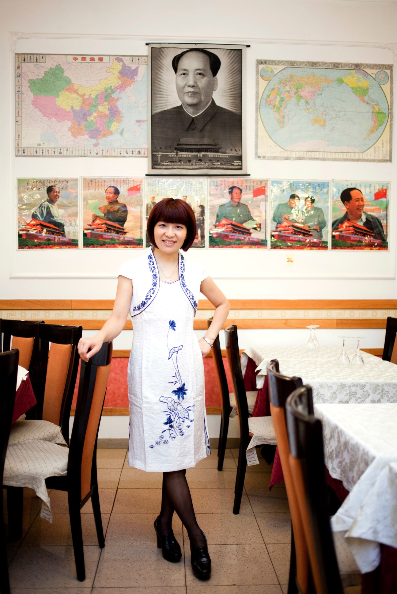 Sonia Hang Zhou poses in her restaurant with Chinese political posters and maps on the wall behind her.