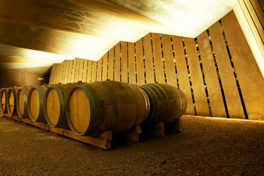 Wine barrels line the interior of a converted bodega with wooden slat walls and warm overhead lighting.