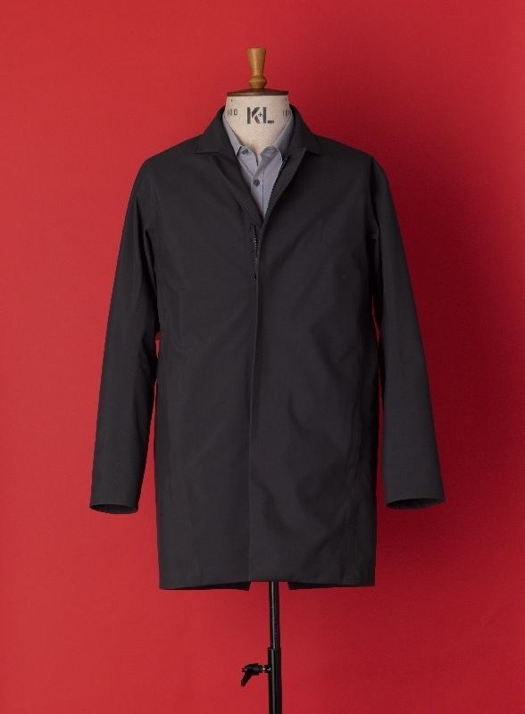 Black Arc'teryx Veilance raincoat displayed on dress form against red background.