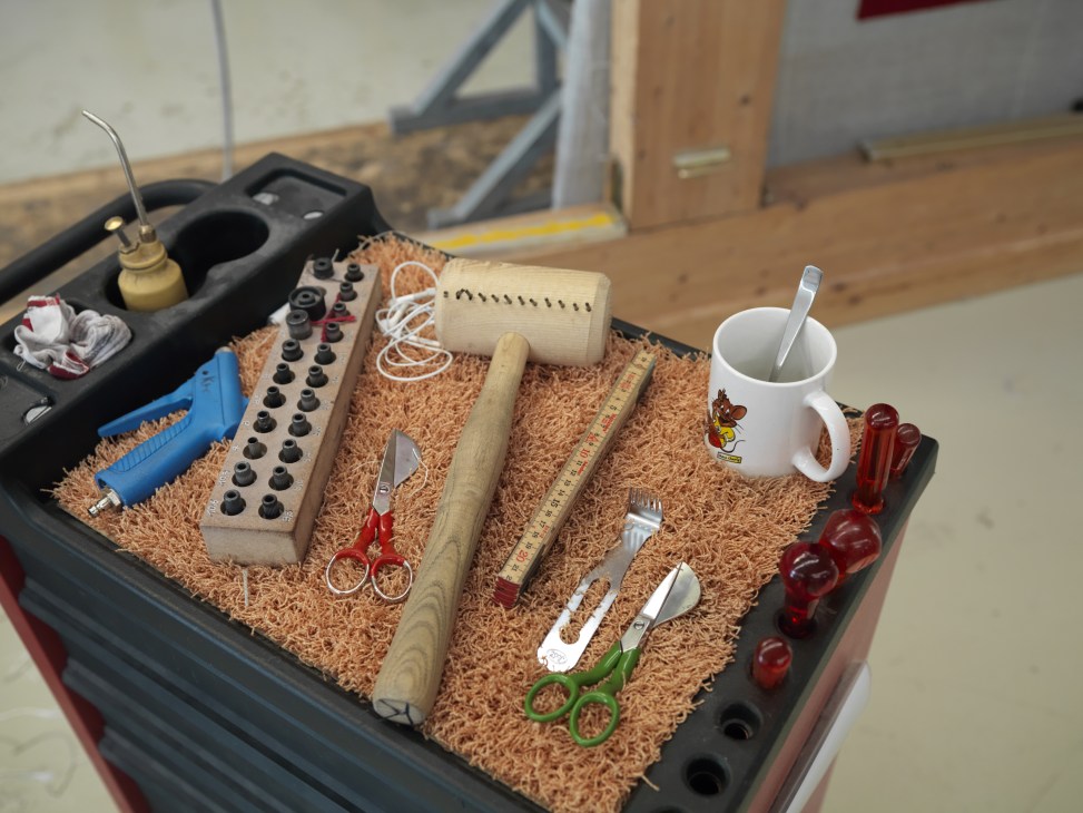 Kramis carpet maker's personal tool kit arranged on carpet wool, including scissors, rulers, hammers, and sketching tools.