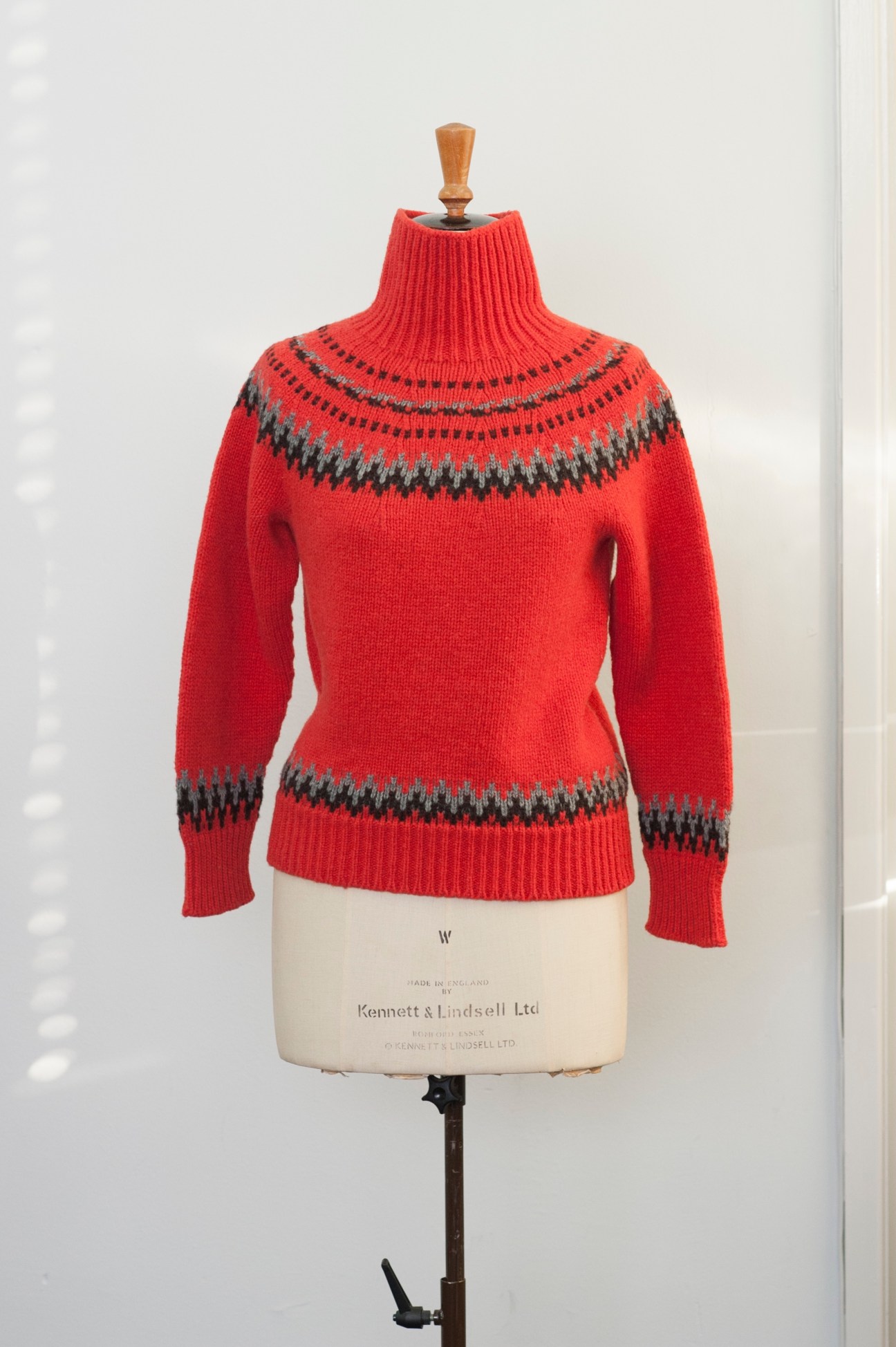 Red knit sweater with gray patterned yoke and cuffs displayed on a dress form.