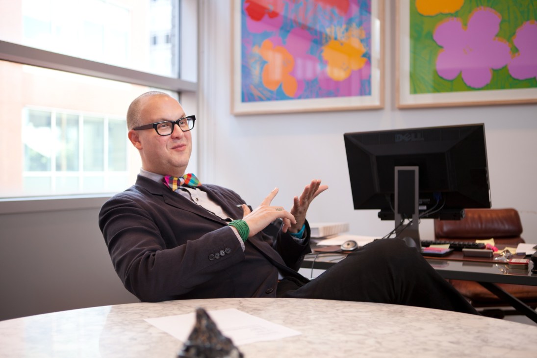 Eric Shiner, director of the Andy Warhol Museum, sits at his desk wearing glasses and a colorful bow tie.