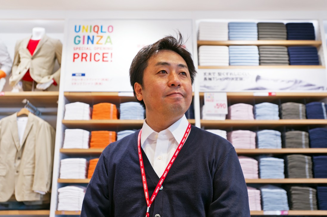 Teruaki Matsumoto, store manager, poses in front of colorful stacked clothing at Uniqlo Ginza.