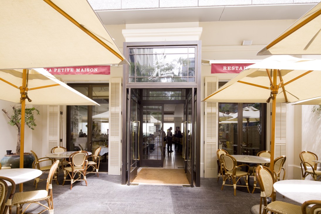 La Petite Maison restaurant exterior in Dubai's DIFC with cream umbrellas and rattan chairs on terrace.
