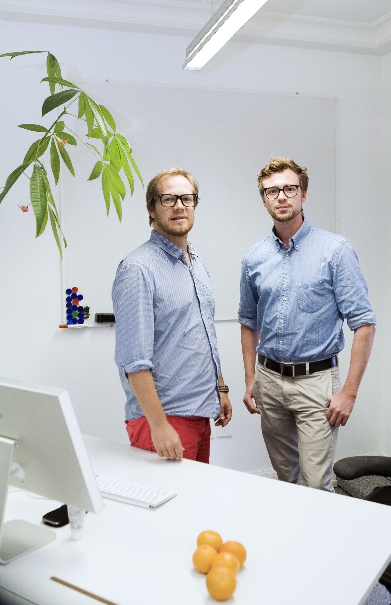 Two graphic designers, Andreas Wester and Jacob Holmberg, stand in a modern office with a potted plant and computer visible.