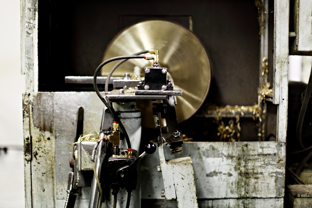 A lathing machine with mechanical components and wiring positioned in front of a large brass cymbal at Zildjian factory.