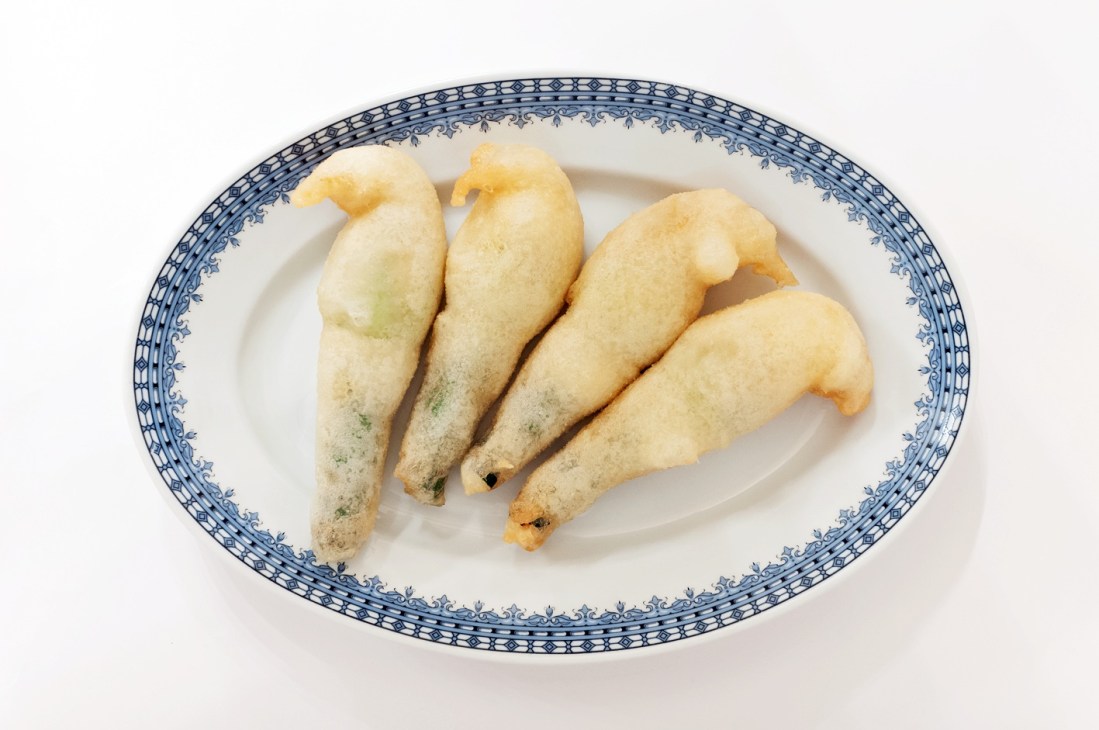 Four golden-fried courgette flower fritters stuffed with mozzarella on a blue-and-white decorative plate.
