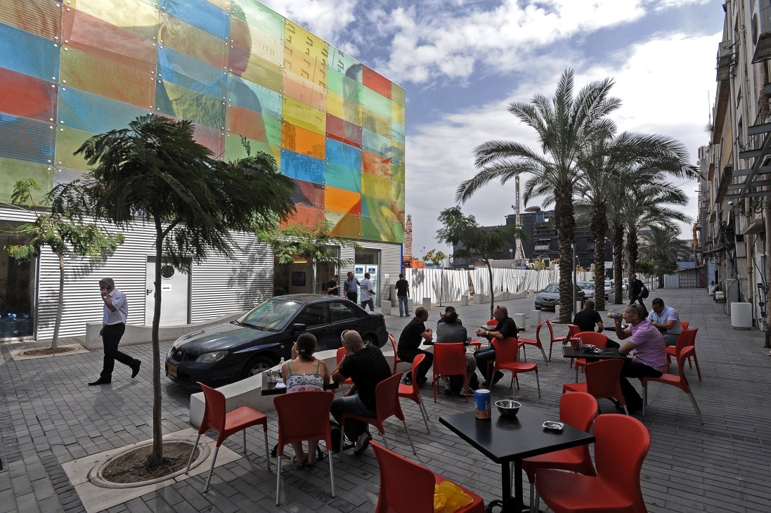 Outdoor café with red chairs in Haifa's Carmel academic centre featuring colorful modern building.