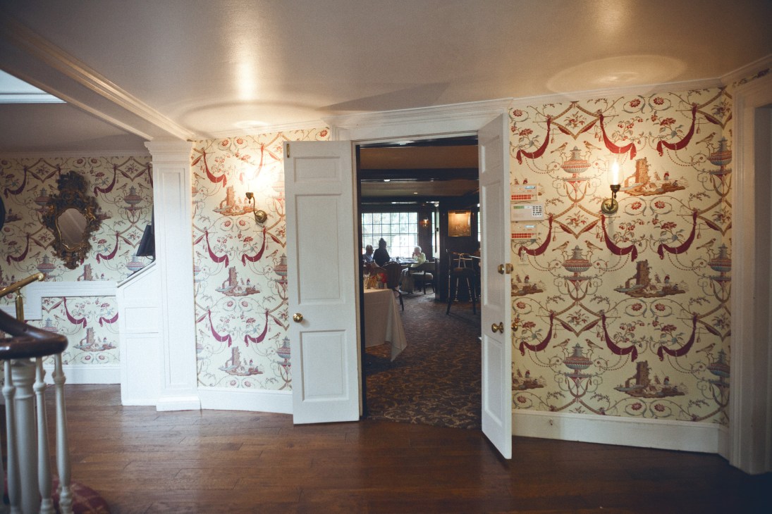 Interior entrance hallway of Roger Sherman Inn with red and cream toile wallpaper and white doors.