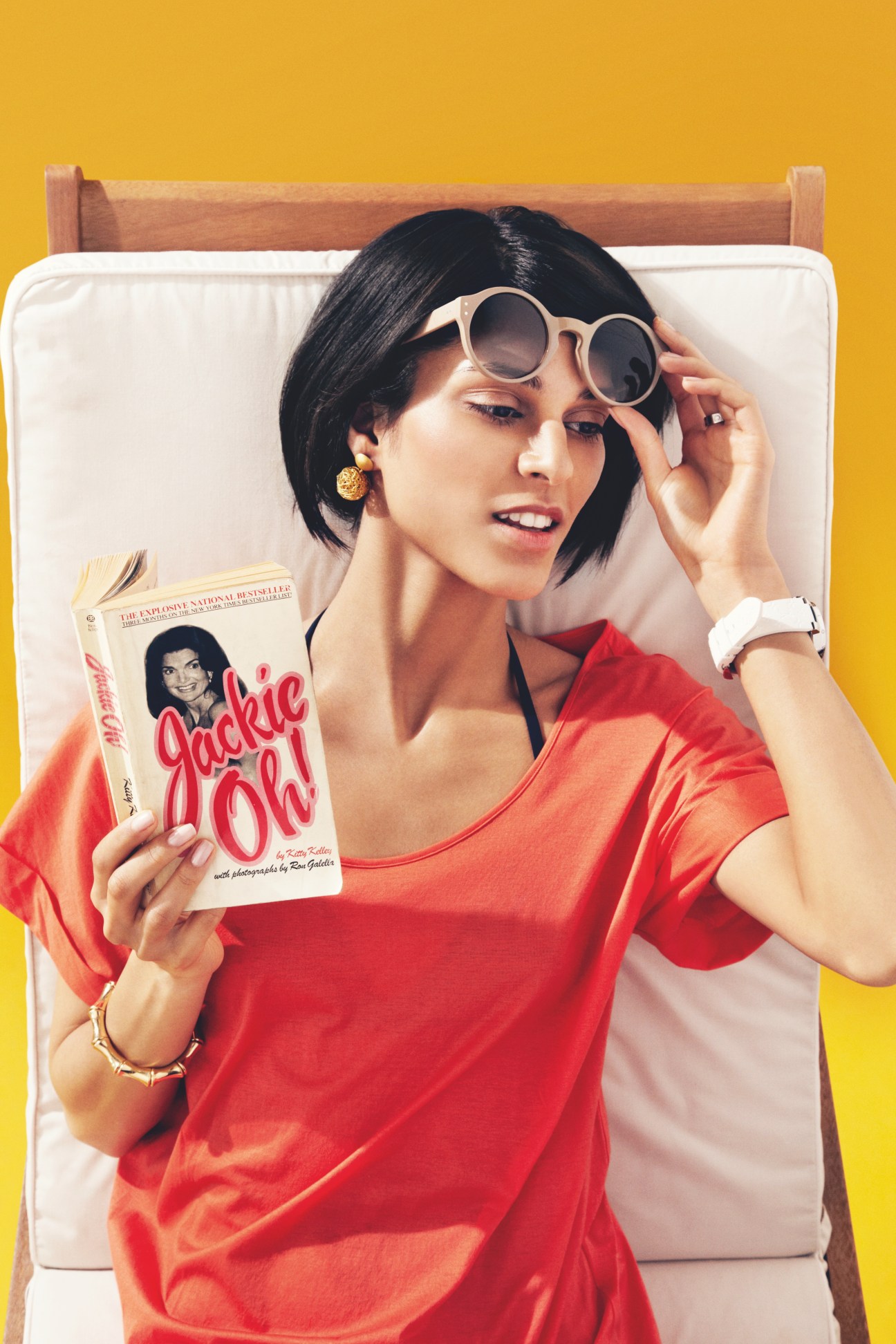 Model wearing Oliver Goldsmith sunglasses and red shirt on lounger with book