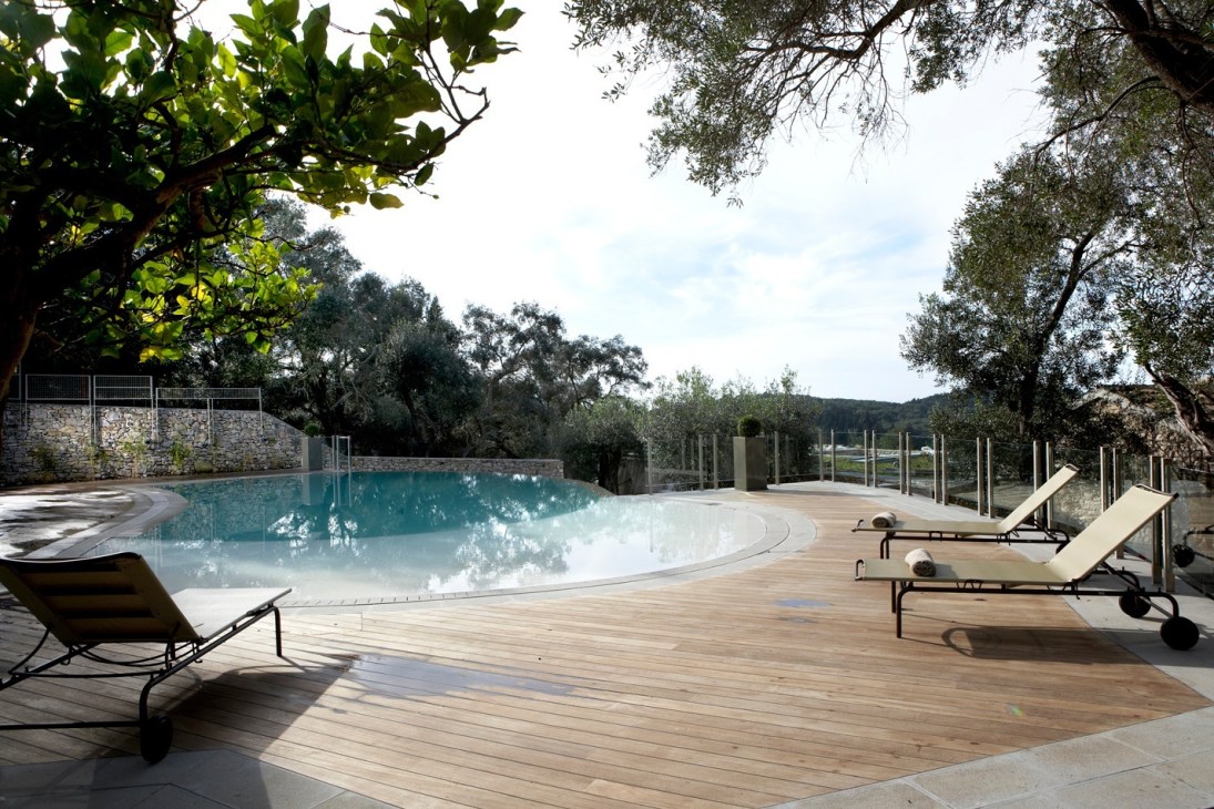 Swimming pool with wooden deck, lounge chairs, and surrounding stone walls with olive trees at Torri e Merli hotel.