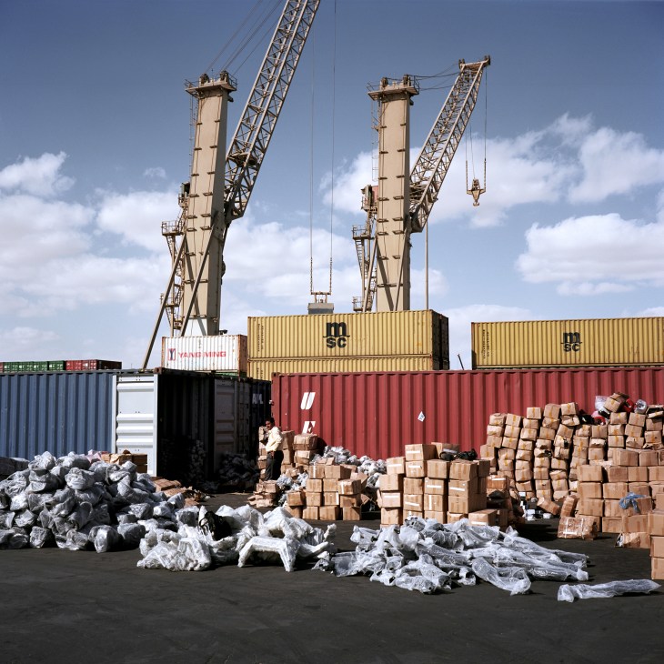 Shipping containers and cargo stacked at DP World Sokhna port with industrial cranes overhead.