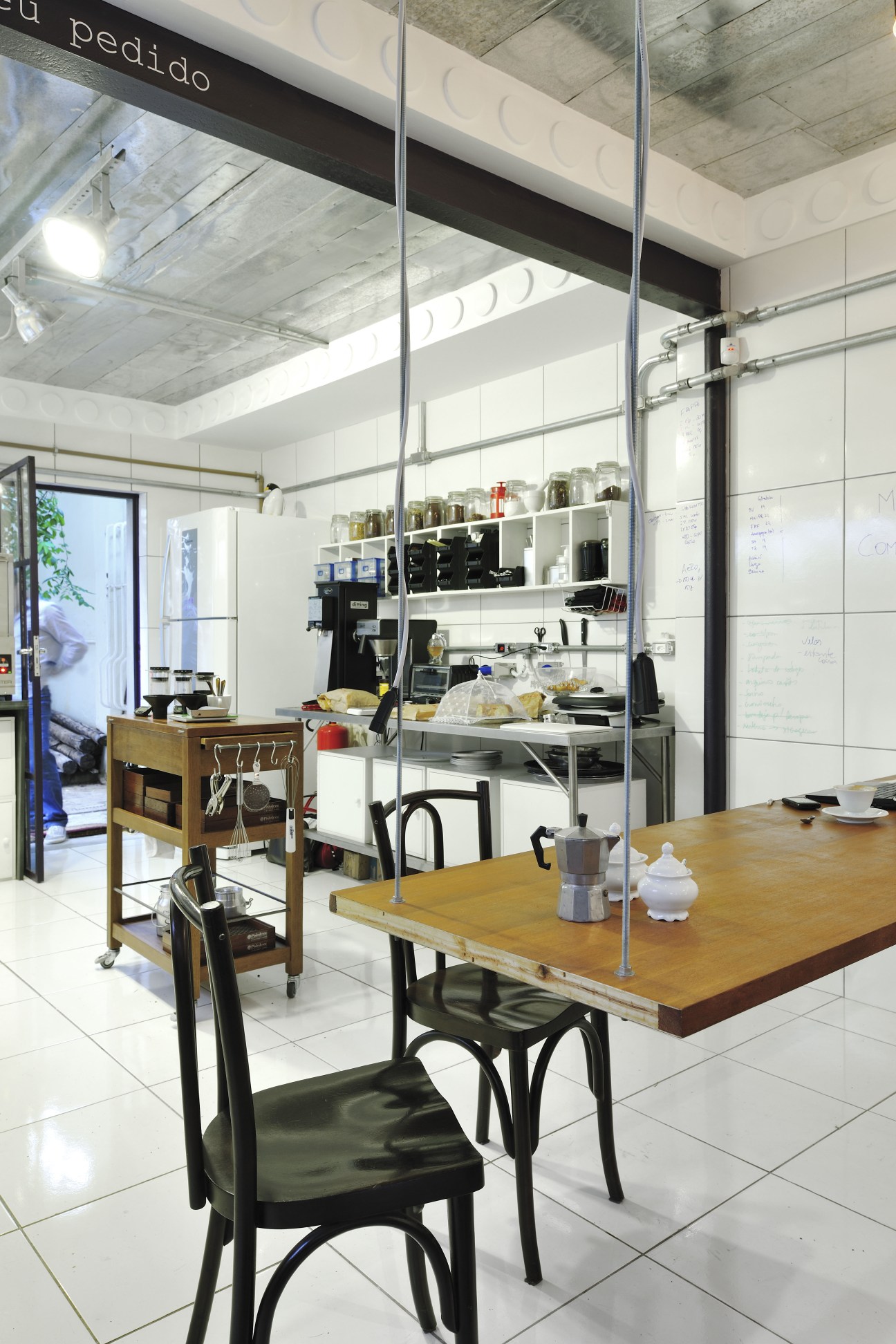 Interior of Coffee Lab roastery and café in São Paulo with wooden table, black chairs, and organized shelving with coffee equipment and jars.