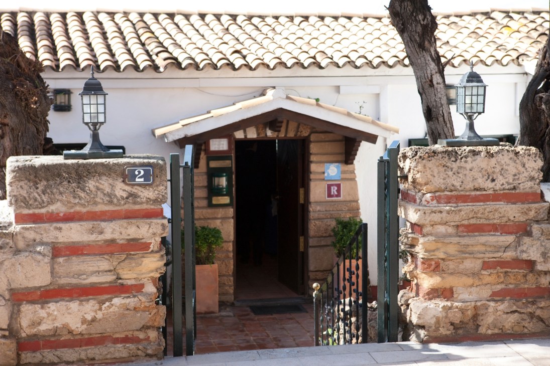El Bungalow entrance with weathered stone walls, wooden door, and traditional Spanish tile roof.