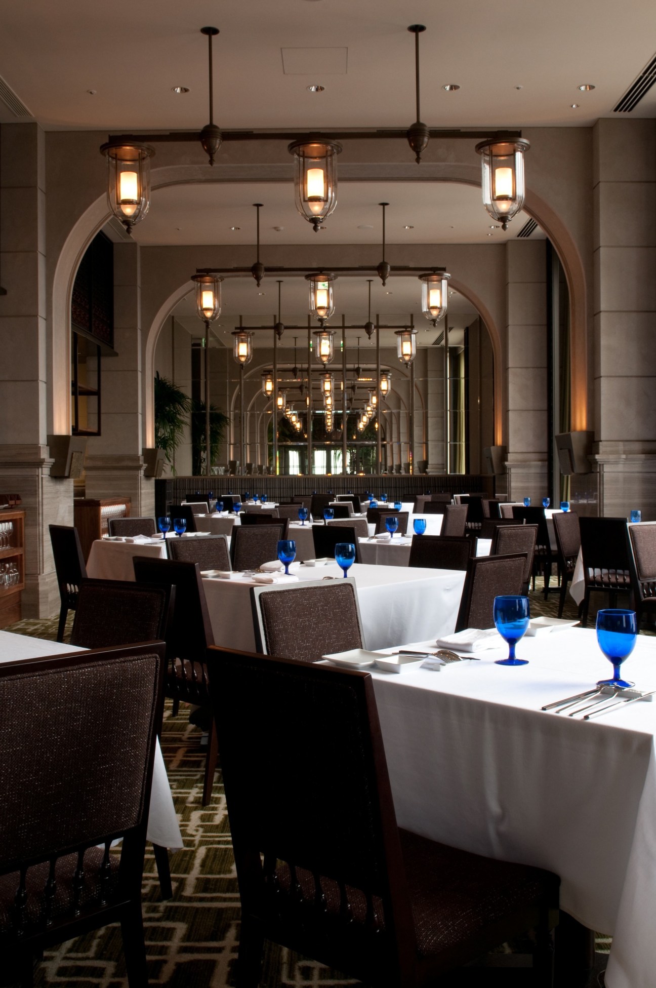 Oriental Hotel restaurant with elegant pendant lights, arched ceilings, white tablecloths and blue glassware.
