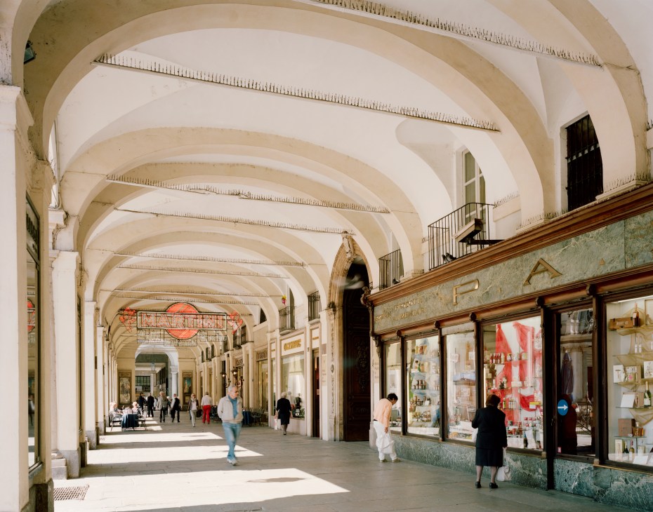Arched covered arcade with cream vaulted ceiling, shop windows, and pedestrians at Piazza San Carlo, Turin.
