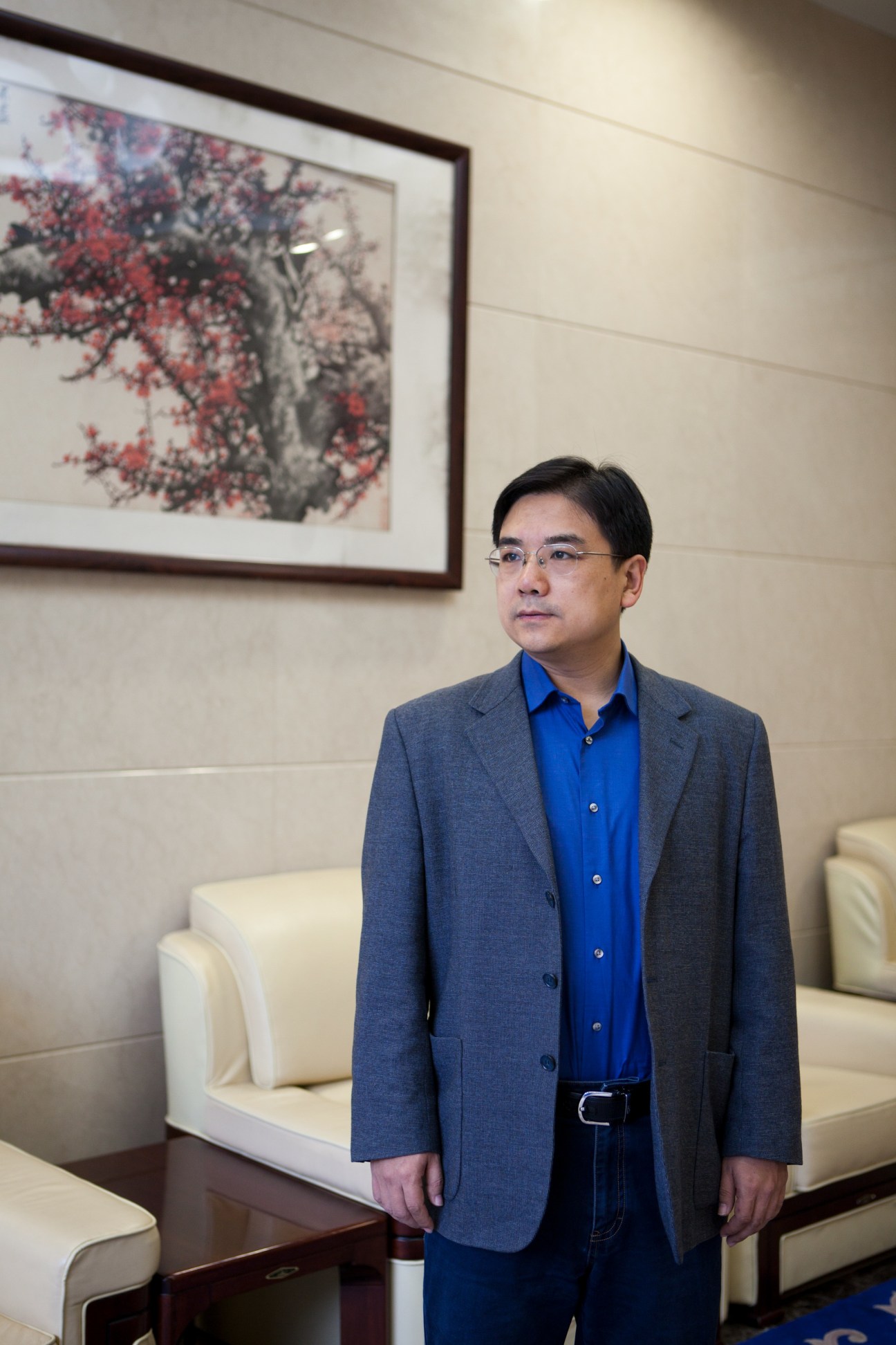 Mi Ligong, director general of CNC, standing in an office with modern furniture and framed artwork on the wall.