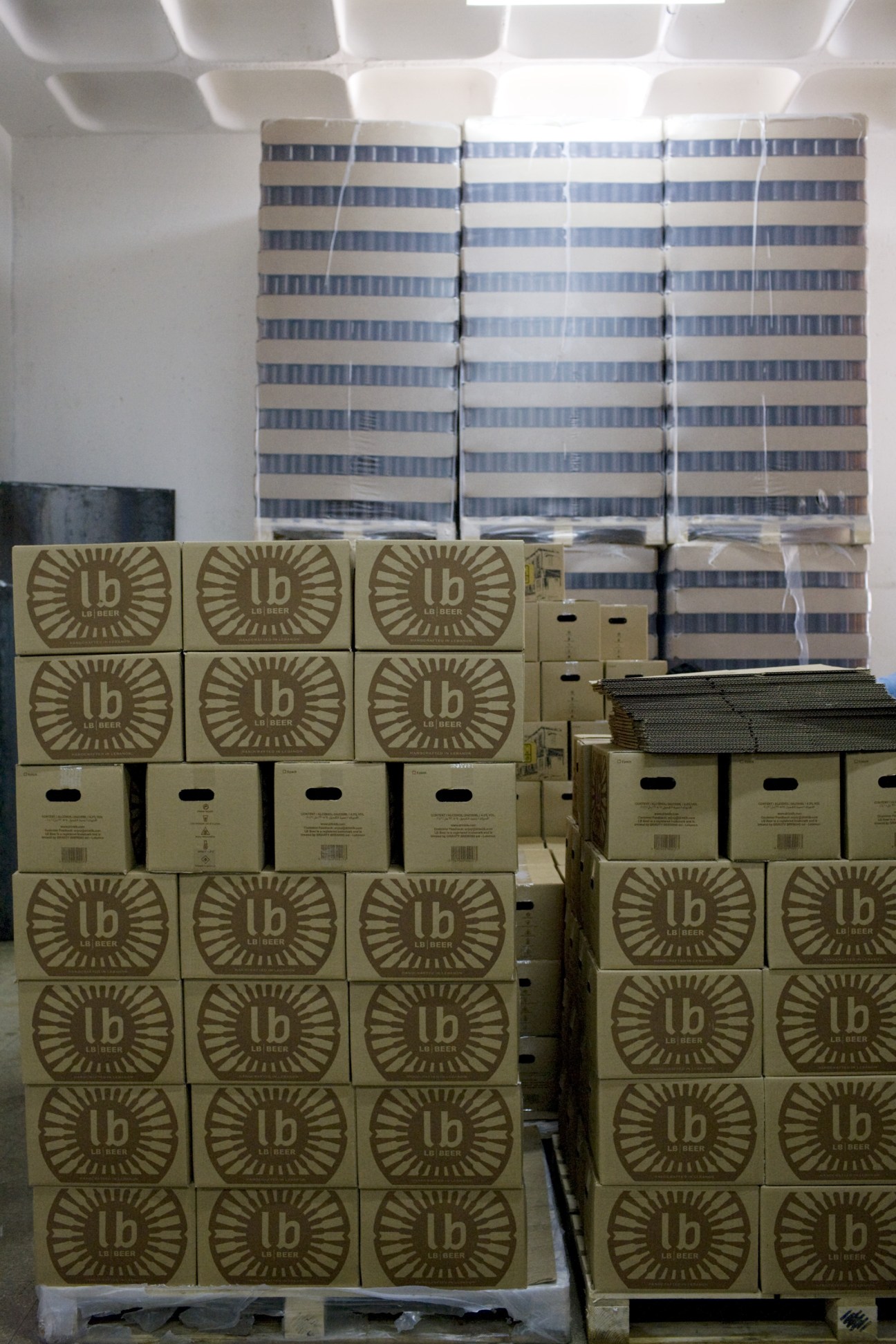 Stacked cardboard cases of LB beer with sun logo symbol in a warehouse.