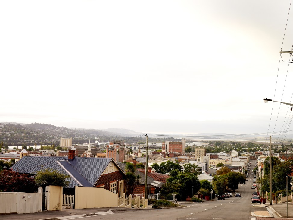 Aerial view of Launceston, Tasmania showing residential and industrial buildings with hills and water in the distance.