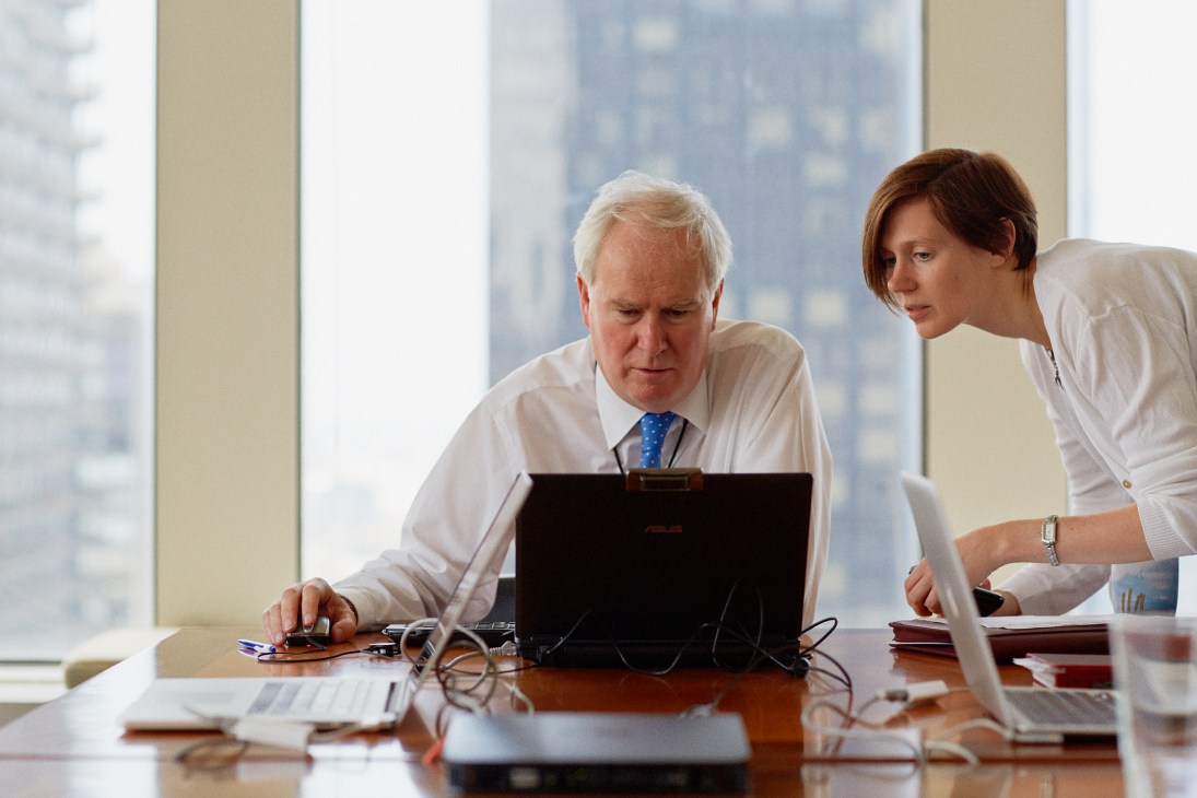 UK ambassador Mark Lyall Grant and head of press Iona Thomas work at a laptop in a high-rise UN office overlooking New York City.