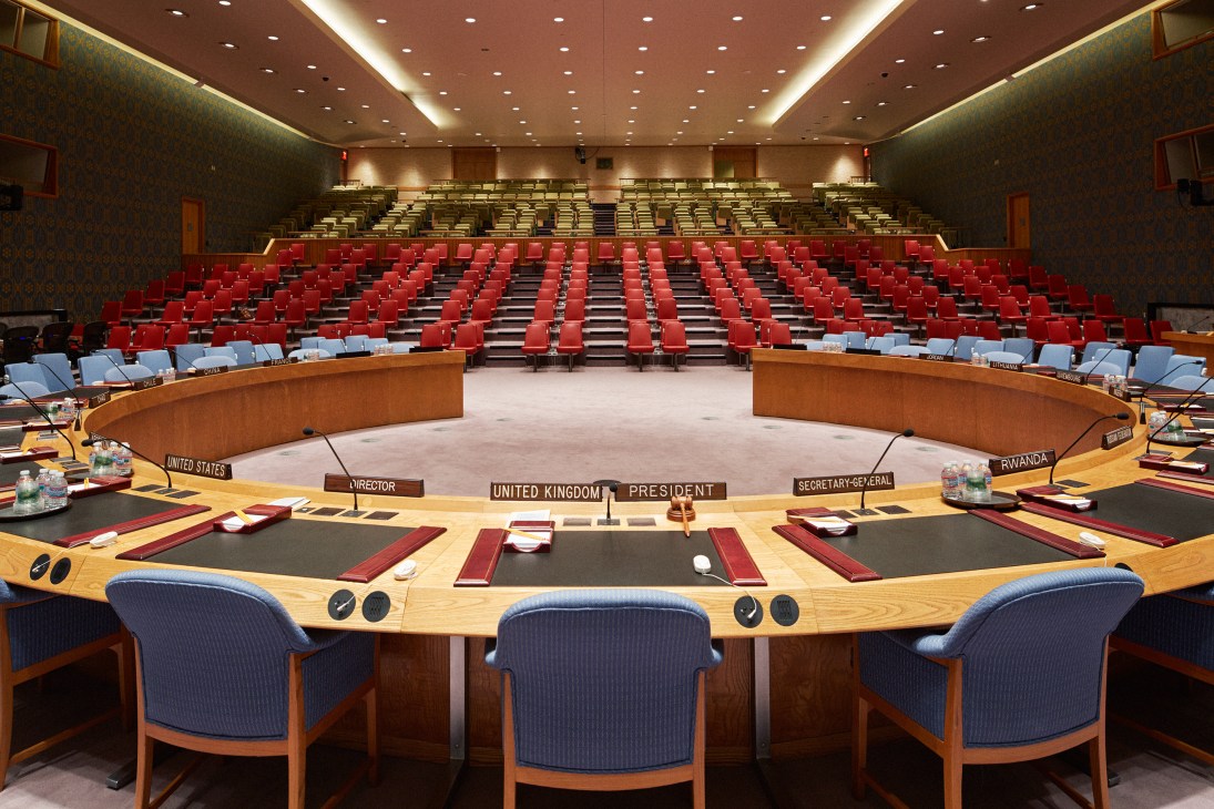 Empty UN Security Council chamber with horseshoe-shaped table and seating for delegates and observers.