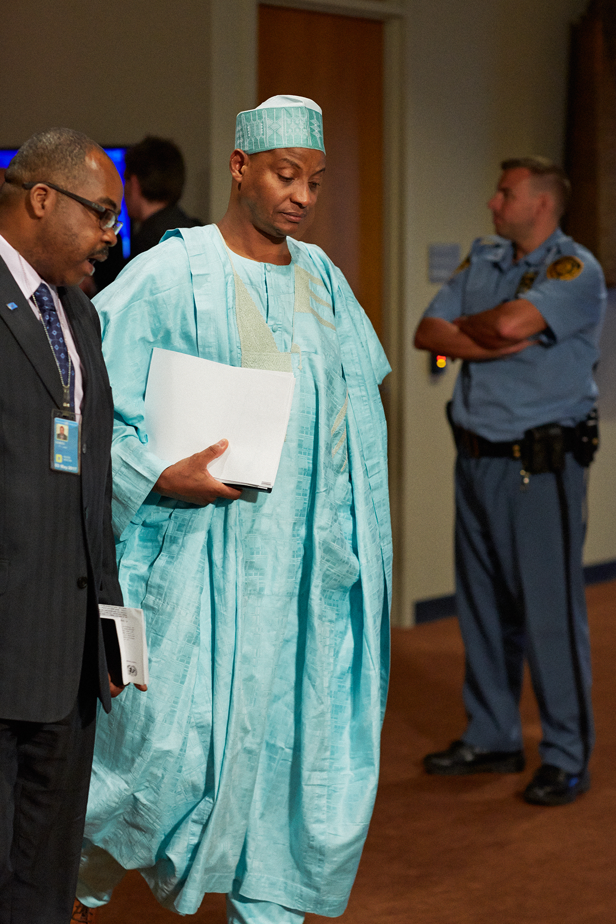 Nigerian delegation member in traditional light blue attire holding documents, departing UN Security Council chamber.