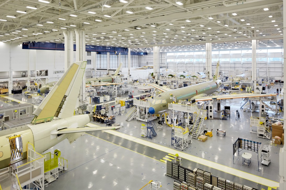 Large aircraft manufacturing hangar with C Series planes in various stages of assembly
