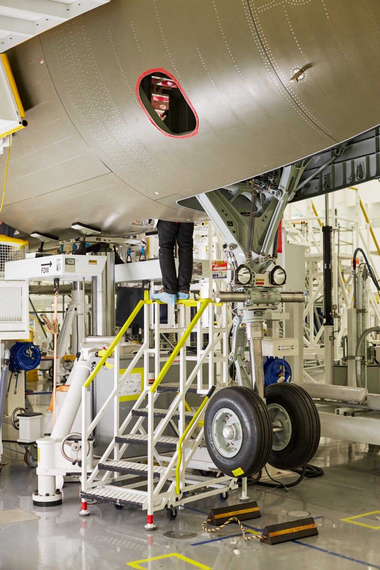 Aircraft maintenance worker on platform working under aircraft fuselage with landing gear visible