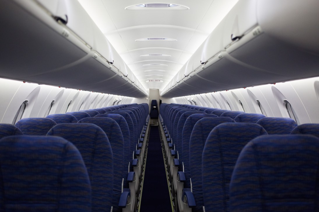 Aircraft cabin interior with blue fabric seats arranged in rows down a white-paneled aisle