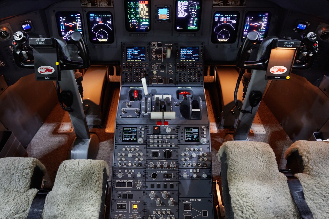 Modern aircraft cockpit with digital displays, control panels, and pilot seats with orange leather upholstery