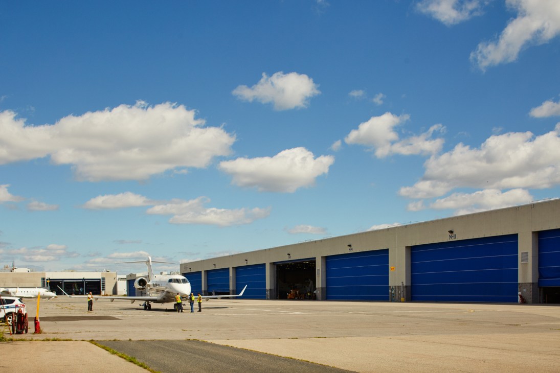 Aircraft hangar with blue doors and white private jet on tarmac under cloudy sky